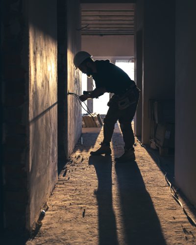 A construction electrician cuts a voltage cable during a repair, silhouette in the light of the setting sun.